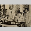 Two men watching another sign a book (ddr-njpa-1-1149)