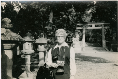 Woman with camera standing by stone lanterns (ddr-densho-426-1073)