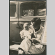 Man holding baby sitting on running board of car (ddr-densho-523-59)