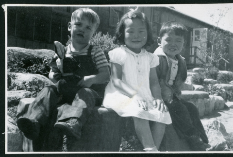 Photograph of children sitting on a bench in front of the Manzanar hospital (ddr-csujad-47-216)
