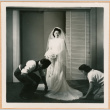 Tomoye (Nozawa) Takahashi smiles for camera while dress is adjusted by man and woman (ddr-densho-410-466)
