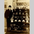Shiro Otsuji posing next to a display case of dolls (ddr-njpa-4-1701)