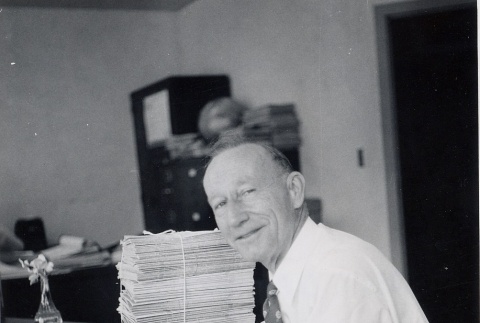 Man seated at desk next to stack of magazines (ddr-njpa-2-426)