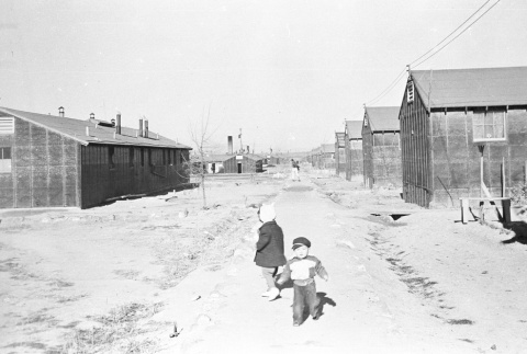 Two children walking between barracks (ddr-densho-39-25)