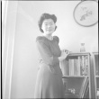 Tomoye (Nozawa) Takahashi standing by bookshelf (ddr-densho-426-2026)