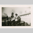 Two women sitting on pile of rocks, barracks in background (ddr-densho-329-1360)