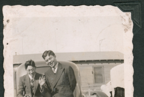 Photo of two men, one leaning on a car and waving at the camera (ddr-densho-483-333)