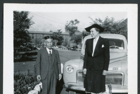 Photograph of a man and L. Josephine Hawes posing next to a car near the Manzanar hospital (ddr-csujad-47-260)