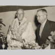 Lester Petrie wearing leis, standing with another man behind a microphone (ddr-njpa-2-812)