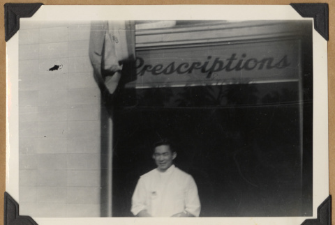 Gary Kikawa posing below a prescriptions sign (ddr-densho-542-164)