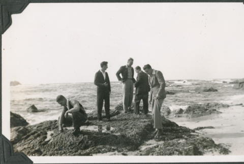 Group of men in civilian clothes standing on rocks by shore (ddr-ajah-2-126)