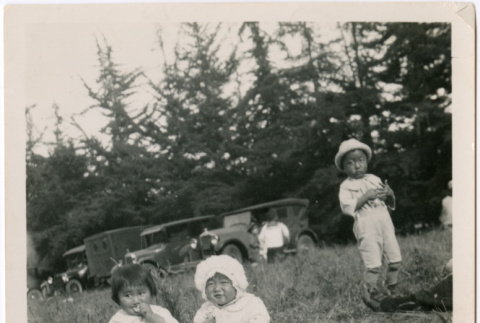 Three children sitting in a field with cars in background (ddr-densho-458-105)