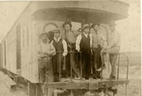 Men standing on the back of a train (ddr-densho-513-4)