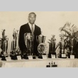 Duke Kahanamoku standing behind a table of trophies (ddr-njpa-2-495)