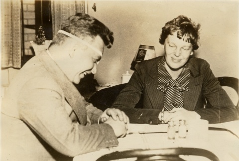 Wiley Post and Amelia Earhart sitting at a table together (ddr-njpa-1-1359)