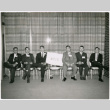 Six men seated, holding ATIS sign (ddr-ajah-2-16)
