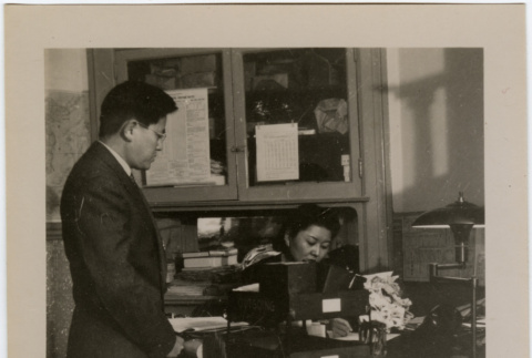 Man standing next to desk, woman seated at desk (ddr-densho-426-945)