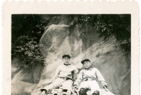 Two boys in baseball uniforms sitting on rocks, man standing on beach (ddr-densho-430-209)