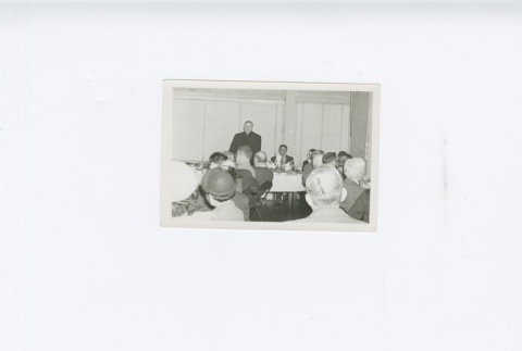 (Photograph) - Image of men and women sitting at tables - Priest standing (ddr-densho-330-282-master-473138ec66)