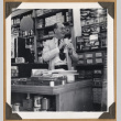 Man standing behind a shop counter (ddr-densho-542-94)