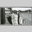 Photograph of four women posing next to a building with two cars in the background at Manzanar (ddr-csujad-47-197)
