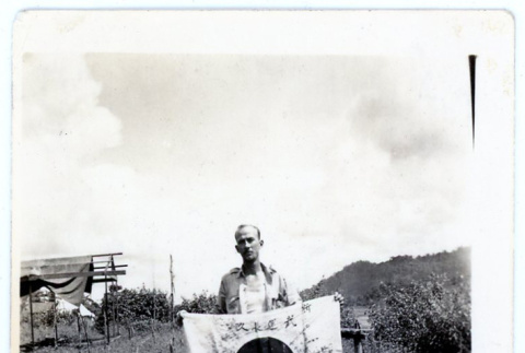 American service man holding Japanese good luck flag (yosegaki hinomaru) (ddr-densho-373-43)