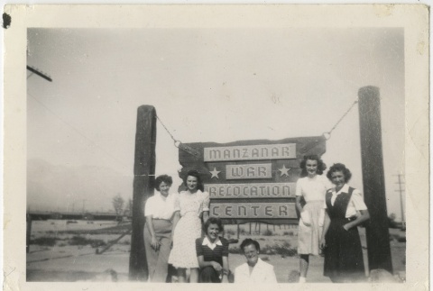 Women in front of camp entrance sign (ddr-manz-7-115)