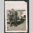Photo of two men, one leaning on a car and waving at the camera (ddr-densho-483-333)