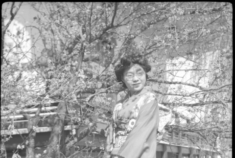 Tomoye (Nozawa) Takahashi in kimono standing by flowering trees (ddr-densho-426-2047)