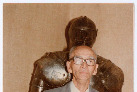 Man posing in front of suit of armor (ddr-densho-501-57)