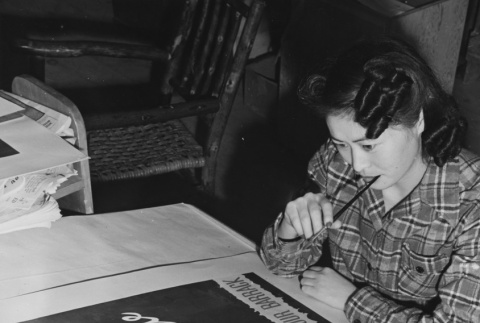 Young artist completing a poster in poster shop at Heart Mountain incarceration camp (ddr-csujad-14-9)
