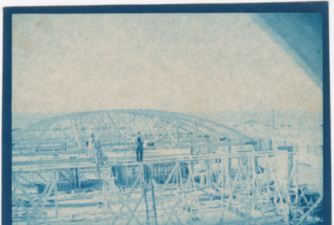 Building site with large wooden structure, men standing on framing (ddr-densho-329-1386)