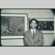 Man standing in front of two framed paintings (ddr-densho-330-154)