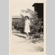 Woman standing in front of trees and barracks (ddr-densho-420-14)
