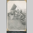Man standing outside mess tent with men eating in background (ddr-densho-434-222)