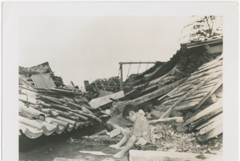 A boy sitting in the rubble of his house after an earthquake (ddr-densho-299-14)