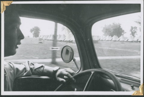 Man behind wheel of car driving past rows of tents (ddr-densho-434-320)