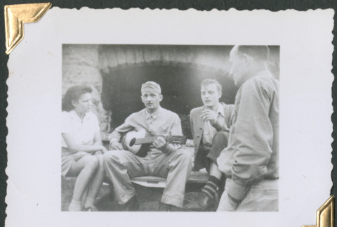 Man playing guitar to two men and a woman (ddr-densho-434-229)