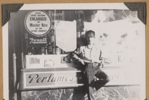 Man poses next to a perfume sign (ddr-densho-542-59)