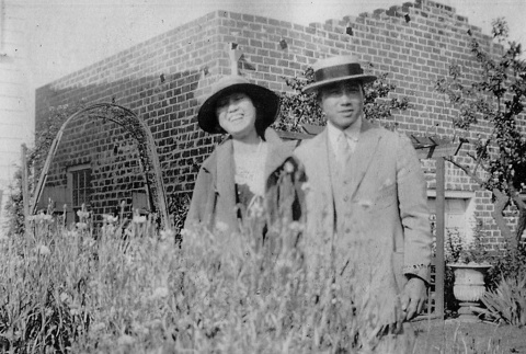Henry and Mitsuyo Takagi in garden outside brick building (ddr-ajah-6-896)