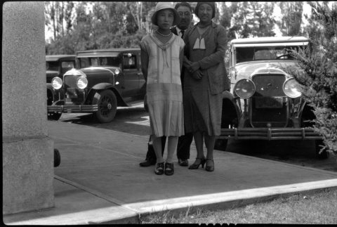 Two women and one man pose in front of cars (ddr-densho-480-21)