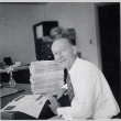 Man seated at desk next to stack of magazines (ddr-njpa-2-426)