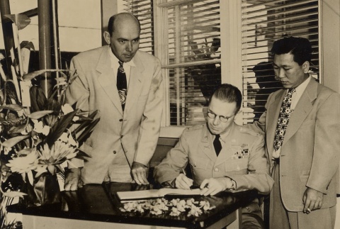 Two men watching another sign a book (ddr-njpa-1-1149)