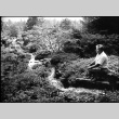 Tom Kubota sitting by Mountainside stream in Garden (ddr-densho-354-2233)