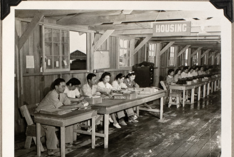 Group seated at row of tables with sign for Housing (ddr-densho-587-80)