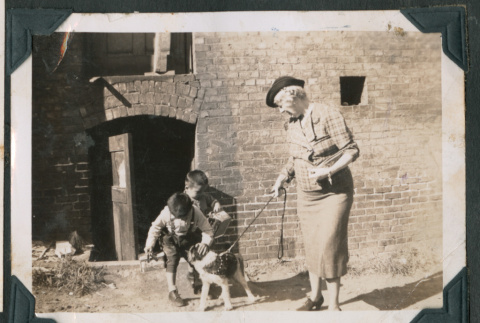 Photo of two children petting a dog held on a leash by an elderly woman (ddr-densho-483-851)