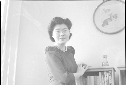 Tomoye (Nozawa) Takahashi standing by bookshelf (ddr-densho-426-2026)