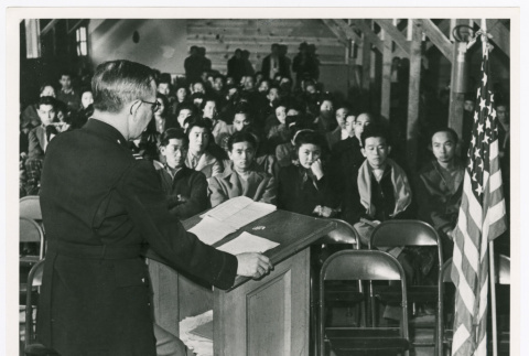 Speaking at podium with flag (ddr-densho-1007-214)