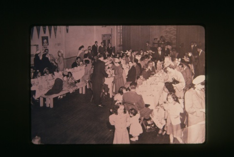 (Slide) - Image of people seated and standing at and around two tables (ddr-densho-330-206-master-5f8479a72f)