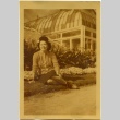 Akiko Sakamoto sitting in front of a greenhouse. (ddr-manz-6-91)